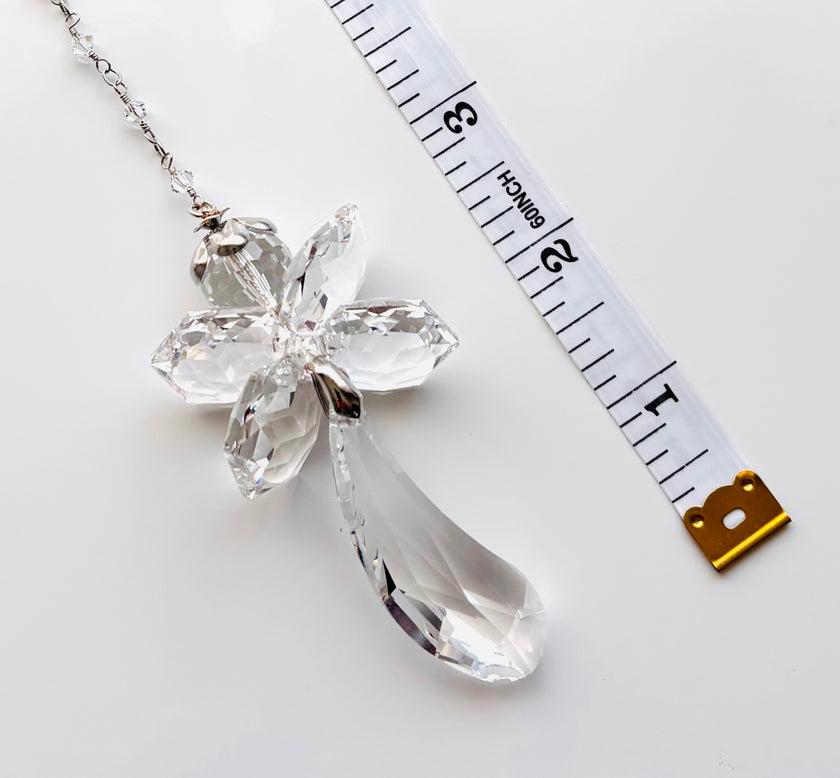 A clear faceted crystal fairy angel showing a teardrop-shaped drop, shown on a white background next to a measuring tape for scale.