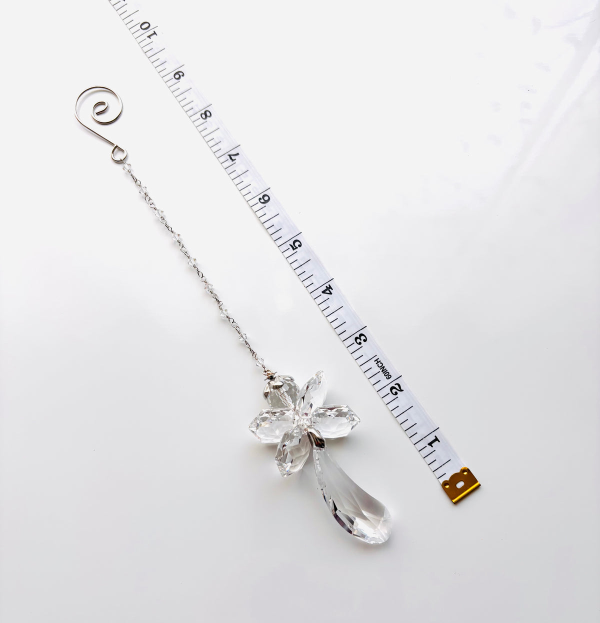 A silver-toned crystal fairy angel with a teardrop crystal pendant and a spiral end, shown next to a measuring tape on a white background.