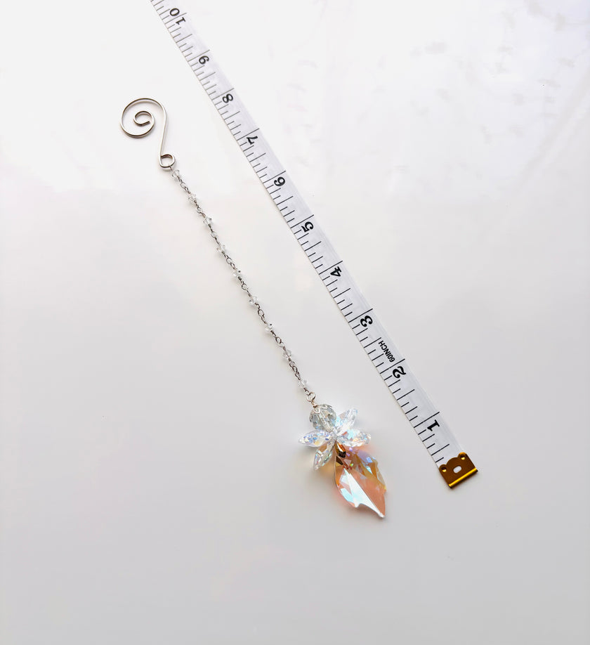 A silver chain with a spiral end, a crystal fairy, and an iridescent pink crystal drop, shown next to a measuring tape on a white background.