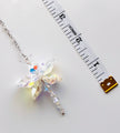 A crystal butterfly pendant necklace on a silver chain, displayed next to a white measuring tape to show its size on a light gray background.