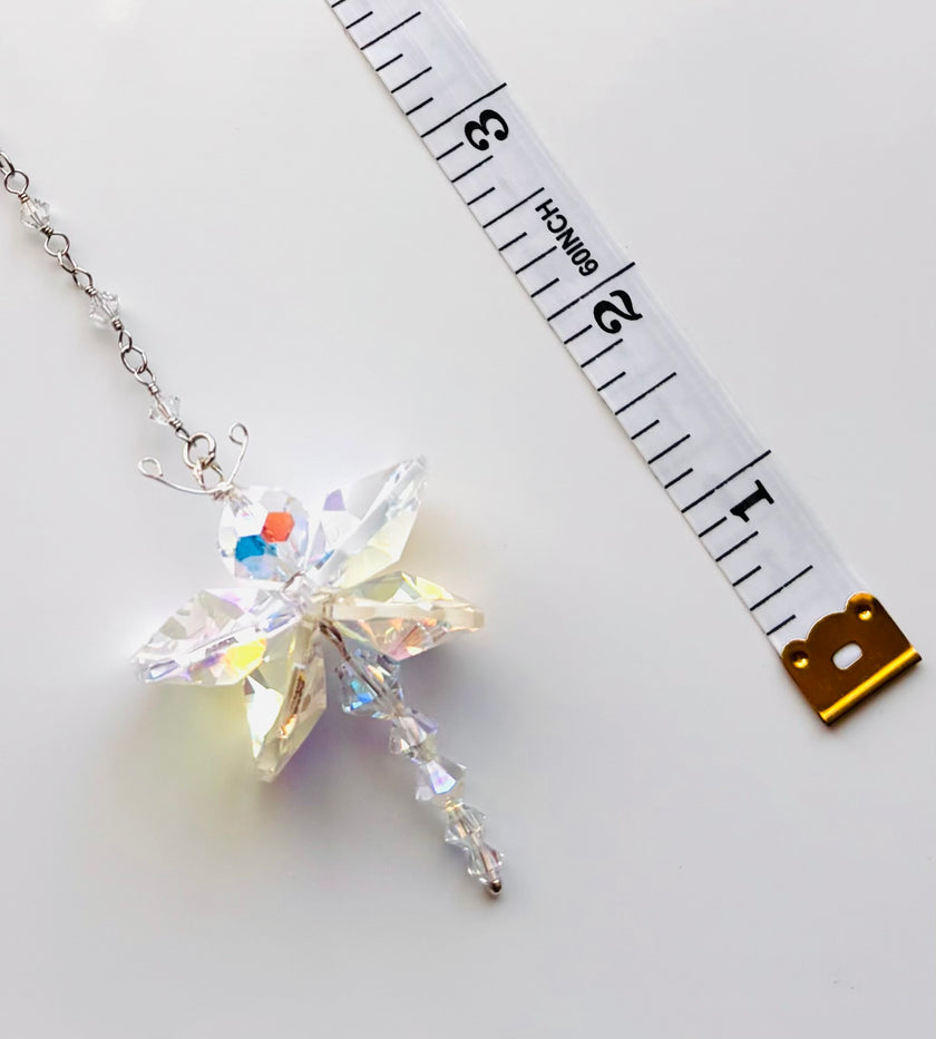 A crystal butterfly pendant necklace on a silver chain, displayed next to a white measuring tape to show its size on a light gray background.