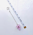 A silver chain with a pink crystal flower fairy pendant and a spiral end, shown next to a white measuring tape on a white background.