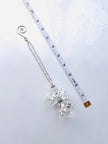 A silver-toned chain accessory with a clear faceted crystal angel pendant and a spiral ring at the top, shown on a white background next to a measuring tape for scale.