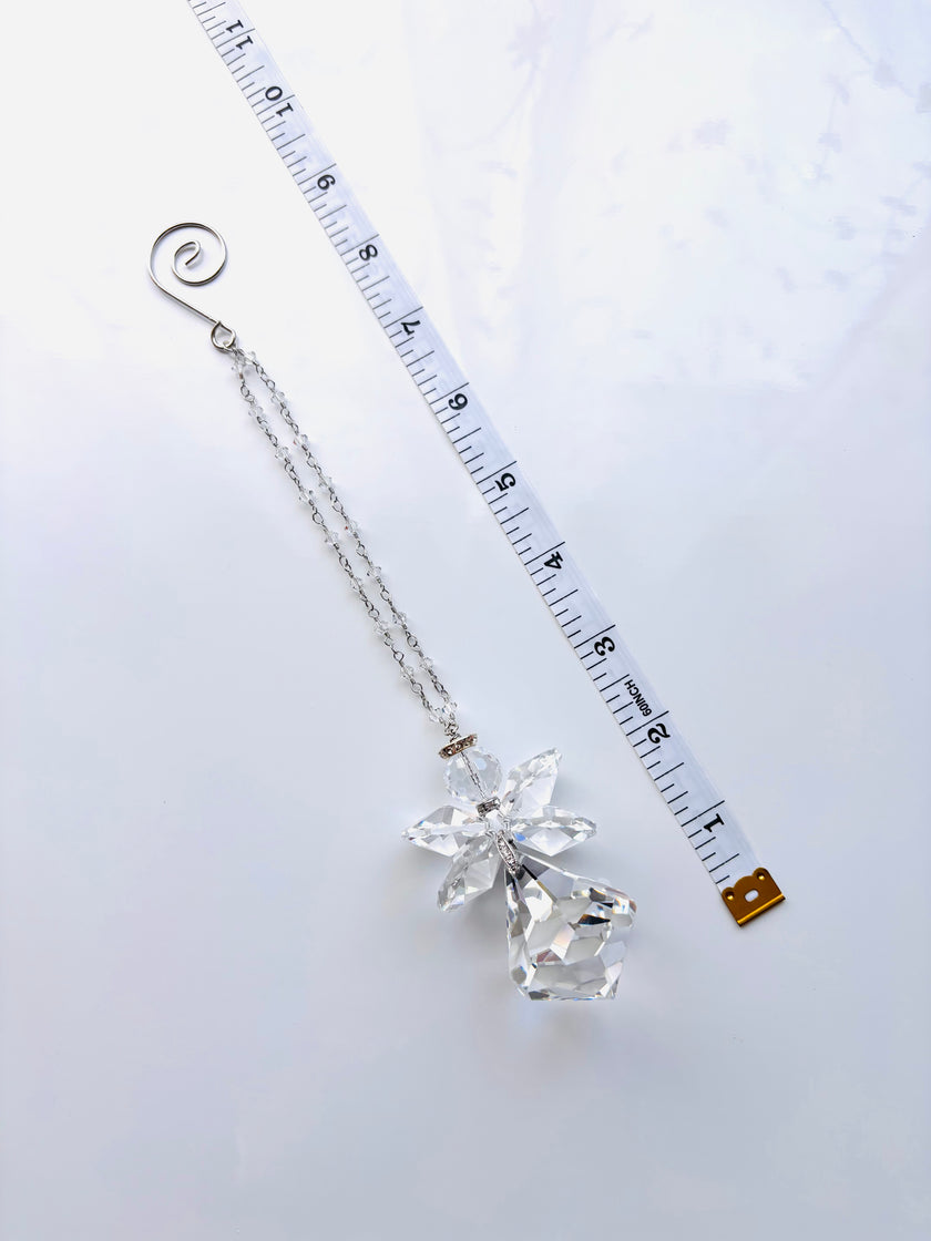 A silver-toned chain accessory with a clear faceted crystal angel pendant and a spiral ring at the top, shown on a white background next to a measuring tape for scale.