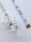 A clear faceted crystal angel pendant necklace with a silver-toned chain, displayed next to a white measuring tape to show scale on a light gray background.