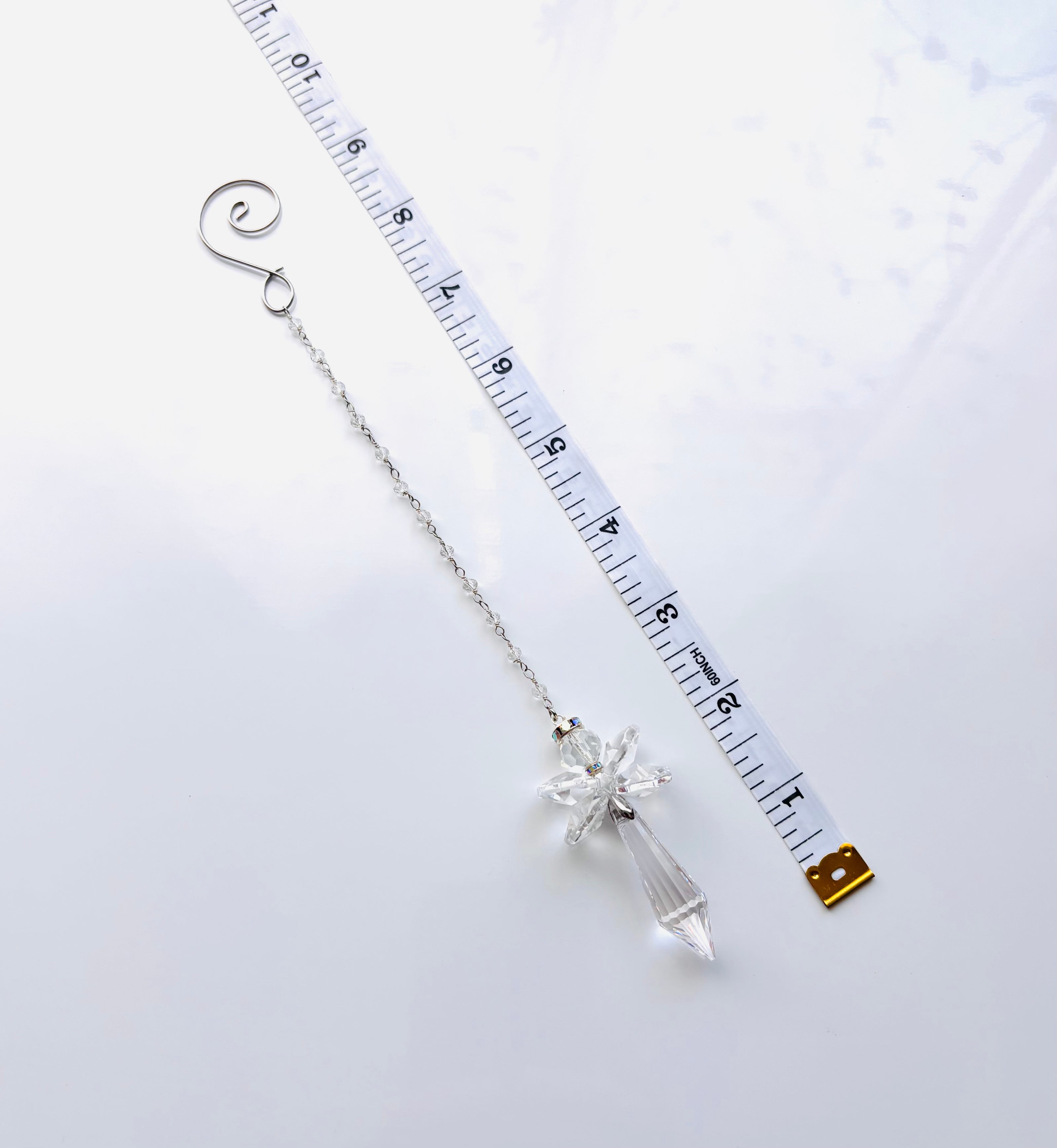 A silver beaded chain with a clear crystal angel shown next to a white measuring tape to indicate its length.