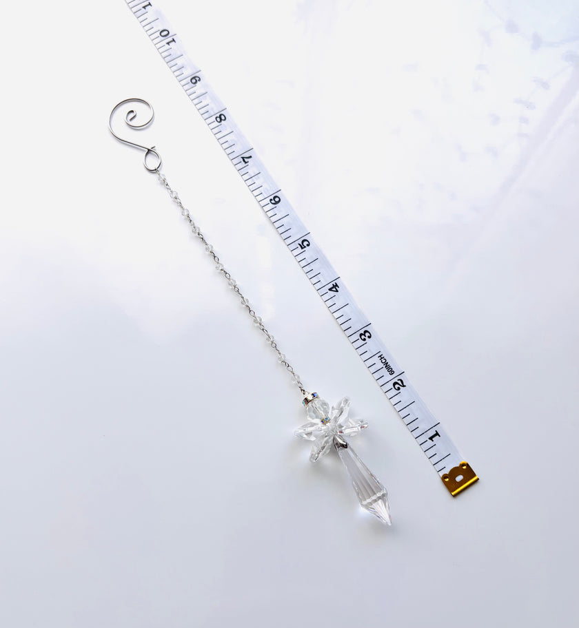 A silver beaded chain with a clear crystal angel shown next to a white measuring tape to indicate its length.