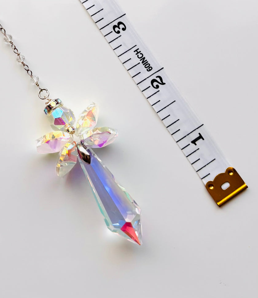An iridescent crystal angel on a silver chain, shown next to a white measuring tape to indicate its size.