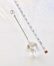 A clear faceted crystal ornament with a silver wire hanger and spiral top, shown on a white marble surface next to a measuring tape for scale.