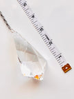 A faceted clear crystal pendant or chandelier drop shown on a white background next to a measuring tape to indicate size.