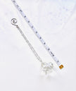 A silver chain with a faceted clear crystal pendant and a spiral clasp, laid diagonally next to a white measuring tape on a white background.