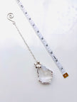 A silver-toned chain with a large baroque, faceted clear crystal pendant, displayed next to a white measuring tape to show scale on a white background.