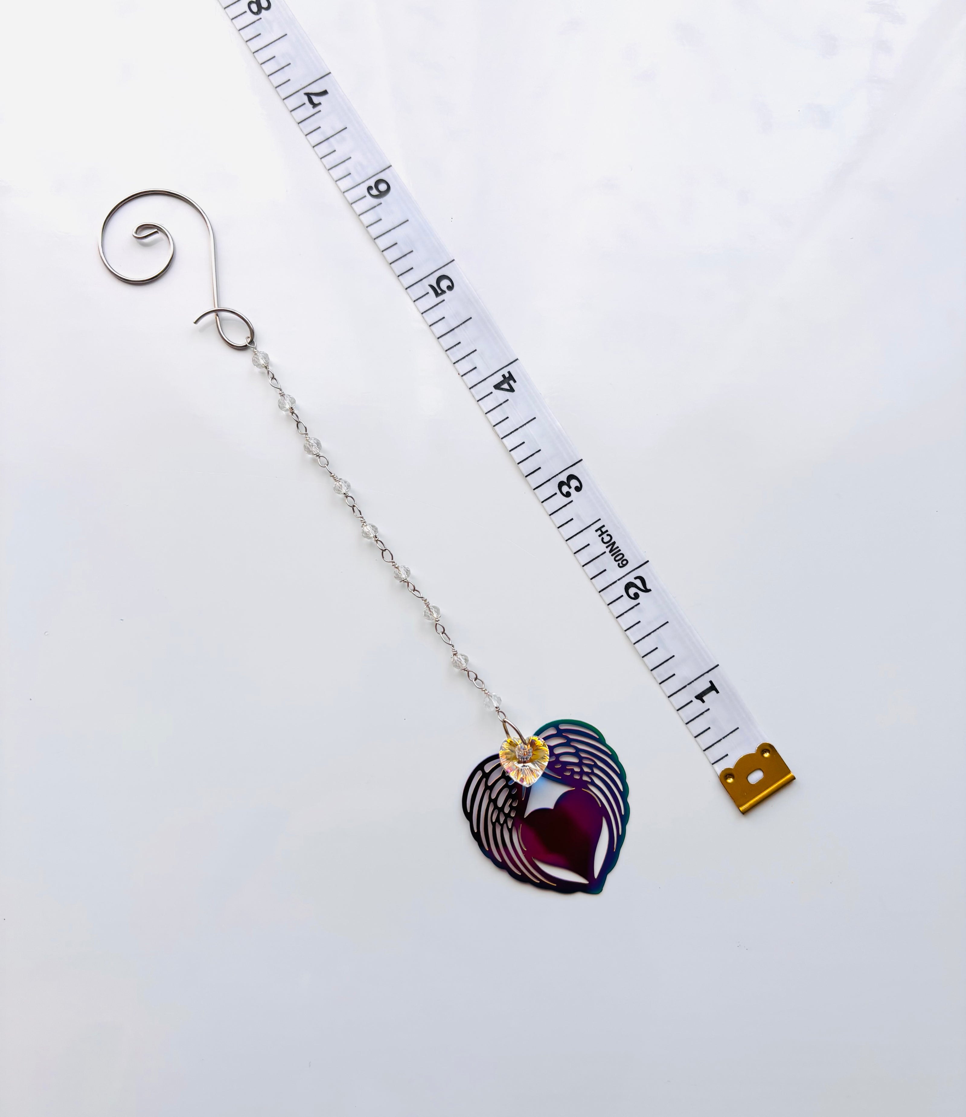 A metallic heart suncatcher on a beaded chain with a measuring tape for dimensions. 