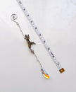 A silver-toned metal suncatcher with a hummingbird with a dangling teardrop crystal pendant, shown next to a measuring tape on a white background.