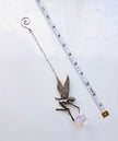 A silver fairy charm with a delicate chain, a small winged fairy pendant, and a clear faceted crystal ball, shown next to a measuring tape on a white background.