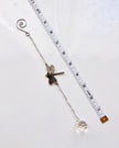 A silver-toned suncatcher featuring a dragonfly charm, a spiral ring at one end, and a faceted clear crystal bead at the other, shown on a white background next to a measuring tape for scale.