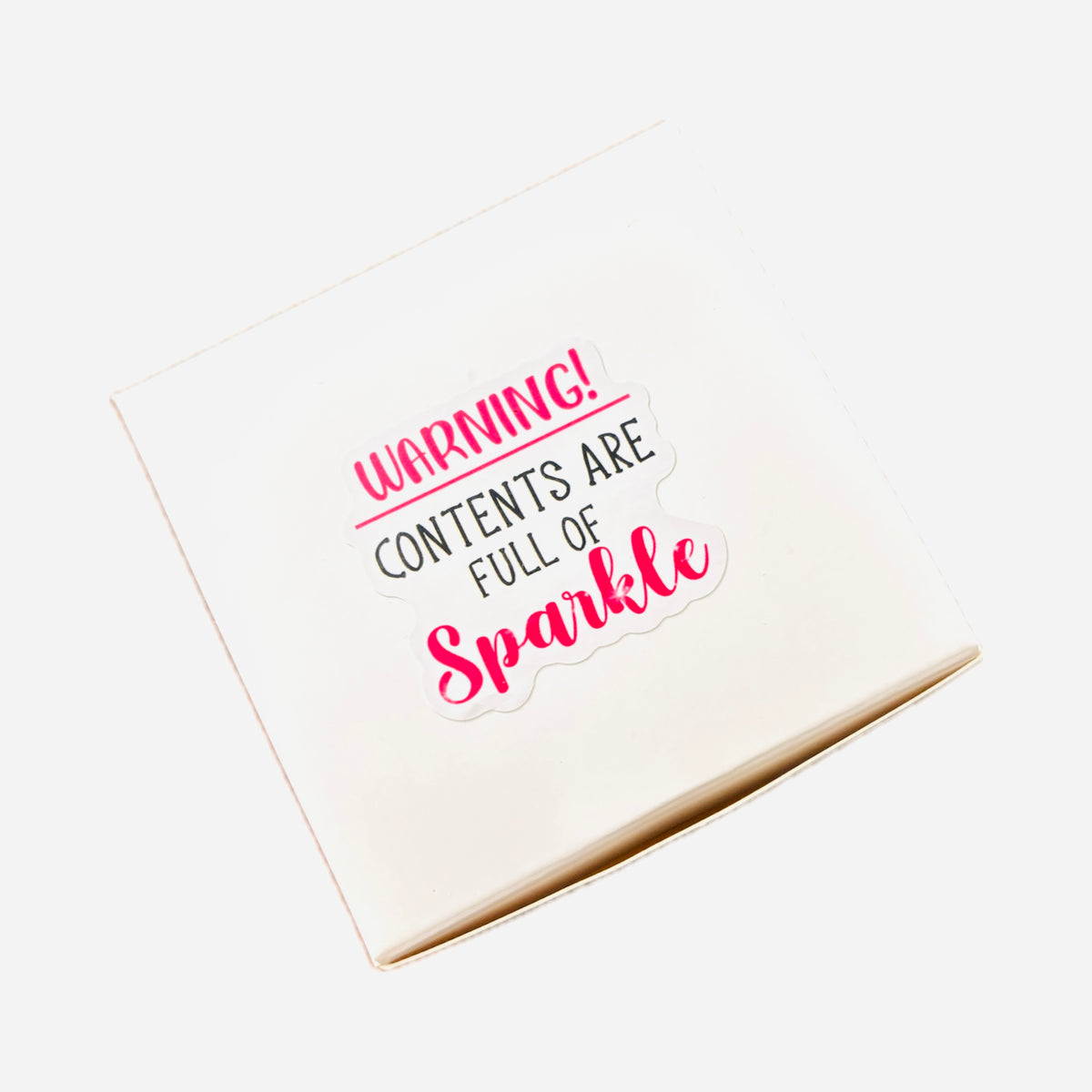 Premium white gift box for the Hopea Swarovski crystal angel suncatcher featuring a playful clear sticker that reads Warning Contents Are Full Of Sparkle in red lettering.