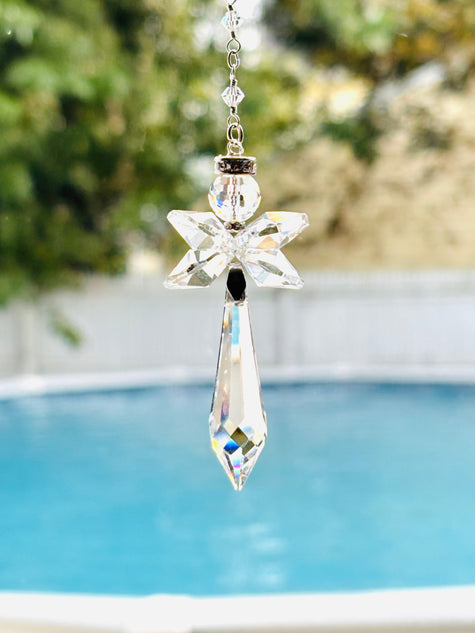 A clear crystal suncatcher with a faceted star and teardrop design hanging outdoors in front of a swimming pool.