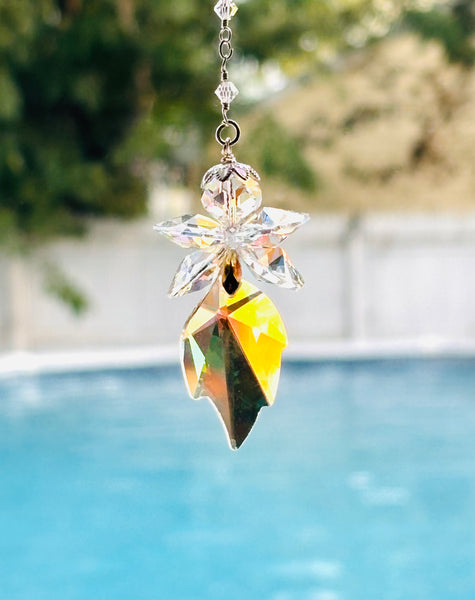A crystal fairy suncatcher with a starburst top and a pointed leaf-shaped bottom, hanging in front of a blurred swimming pool and outdoor background.