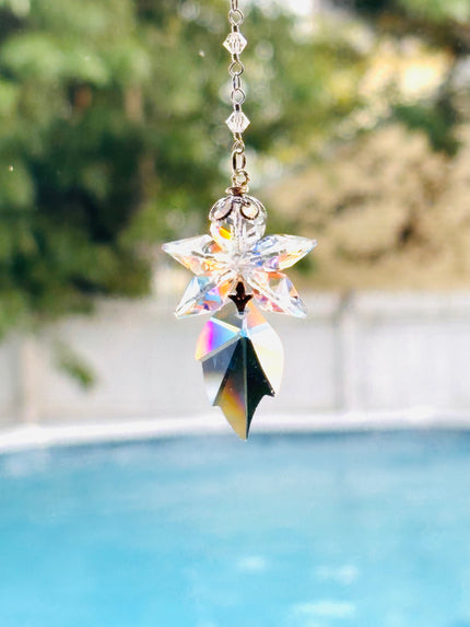 A blue fairy crystal suncatcher with a star-shaped top and a leaf-shaped bottom, made of iridescent clear glass, suspended in front of a blurred outdoor background with a swimming pool.