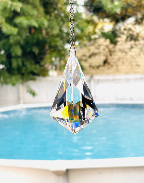 A large faceted clear crystal suncatcher hanging from a silver beaded shimmering with colors in a bright window.