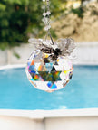 A hanging crystal ball suncatcher with a faceted clear sphere and a silver butterfly ornament shimmering in a bright window.