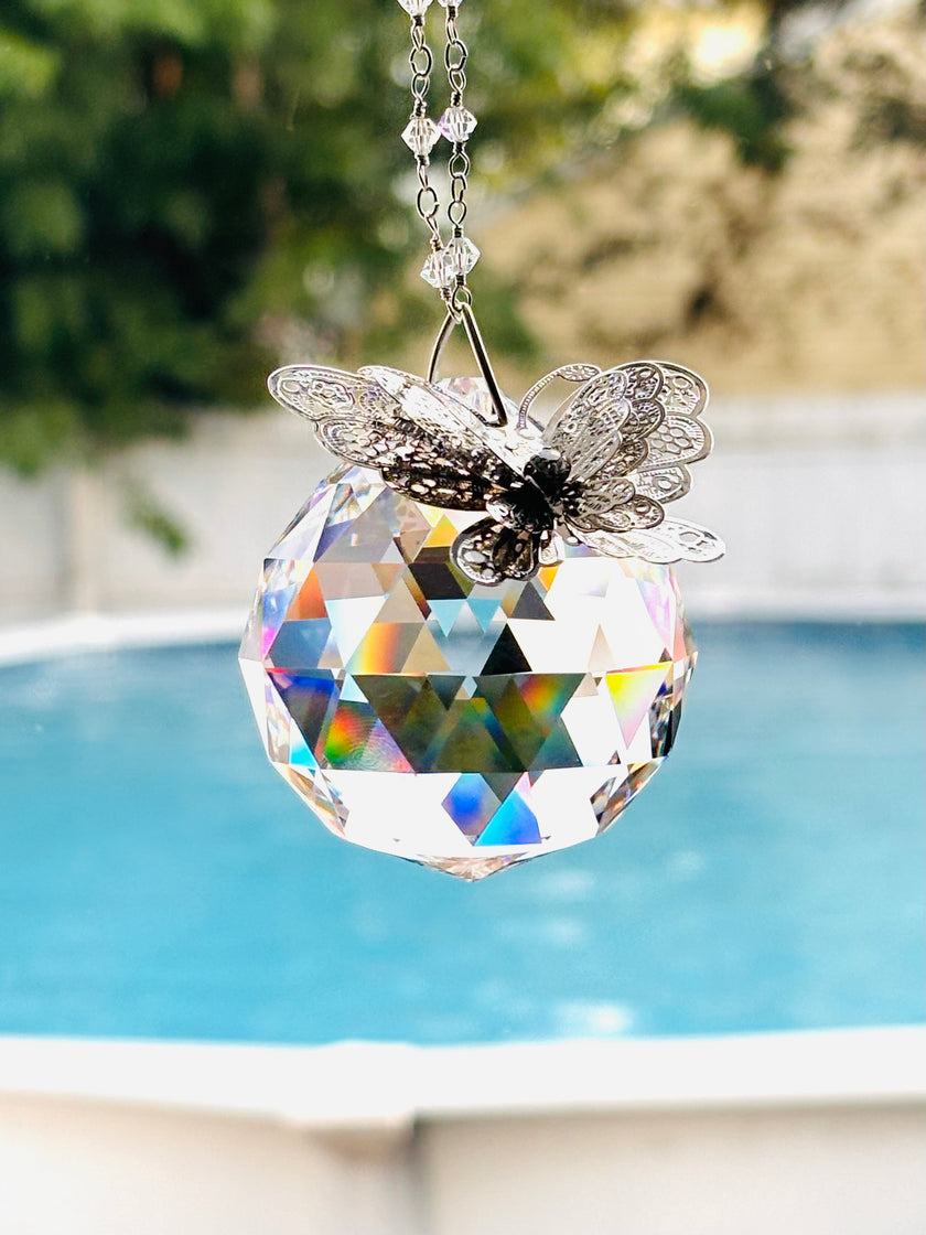 A hanging crystal ball suncatcher with a faceted clear sphere and a silver butterfly ornament shimmering in a bright window.