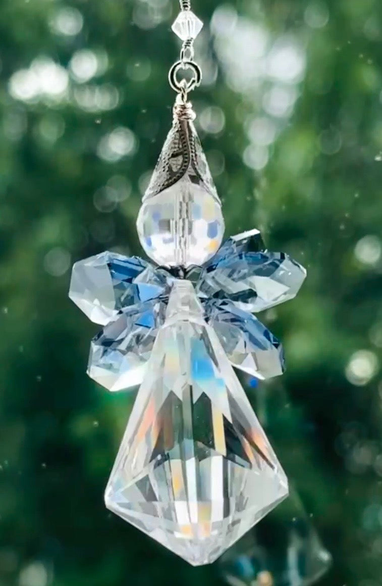 Close-up of the Saphoreus wizard angel crystal suncatcher showcasing the detailed sapphire blue crystal wings and iridescent clear glass body hanging against a sparkly green background.