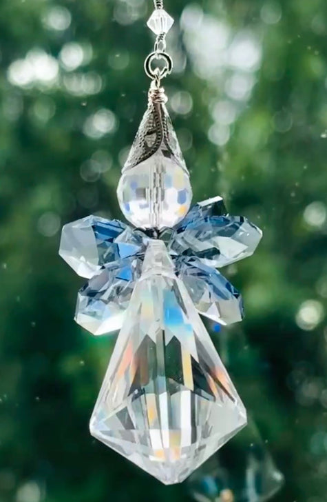 Close-up of the Saphoreus wizard angel crystal suncatcher showcasing the detailed sapphire blue crystal wings and iridescent clear glass body hanging against a sparkly green background.