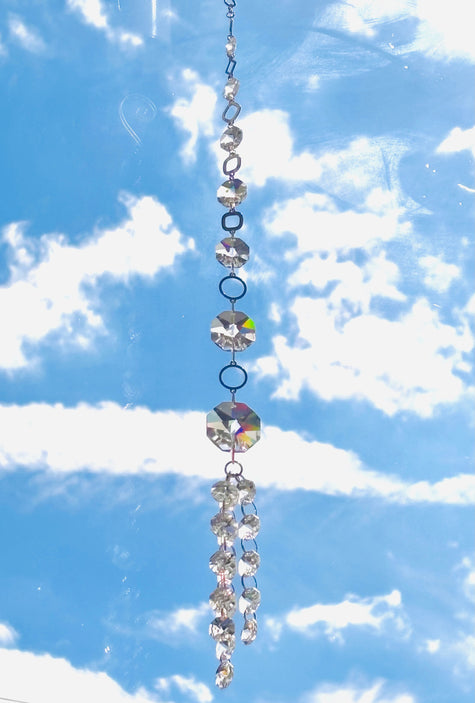  Swarovski crystal suncatcher hanging ornament reflecting light against a scenic blue sky and cloud background.