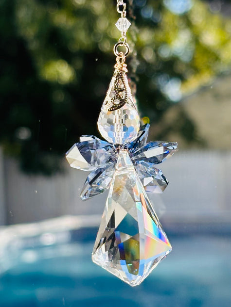 Handcrafted Saphoreus wizard angel crystal suncatcher with sapphire blue wings and a faceted body casting iridescent rainbow prisms over a sunny pool background.