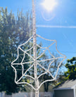 A handmade crystal spiderweb suncatcher being measured vertically with a yellow tape measure outdoors. The tape measure shows the precise scale, width, and hanging dimensions of the full 448-bead crystal web structure against a background of trees.