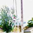 A handmade ASFOUR crystal spider suncatcher being measured vertically with a white tape measure outdoors. The tape measure shows a total hanging length of 13 inches against a bright backdrop of sky and trees.
