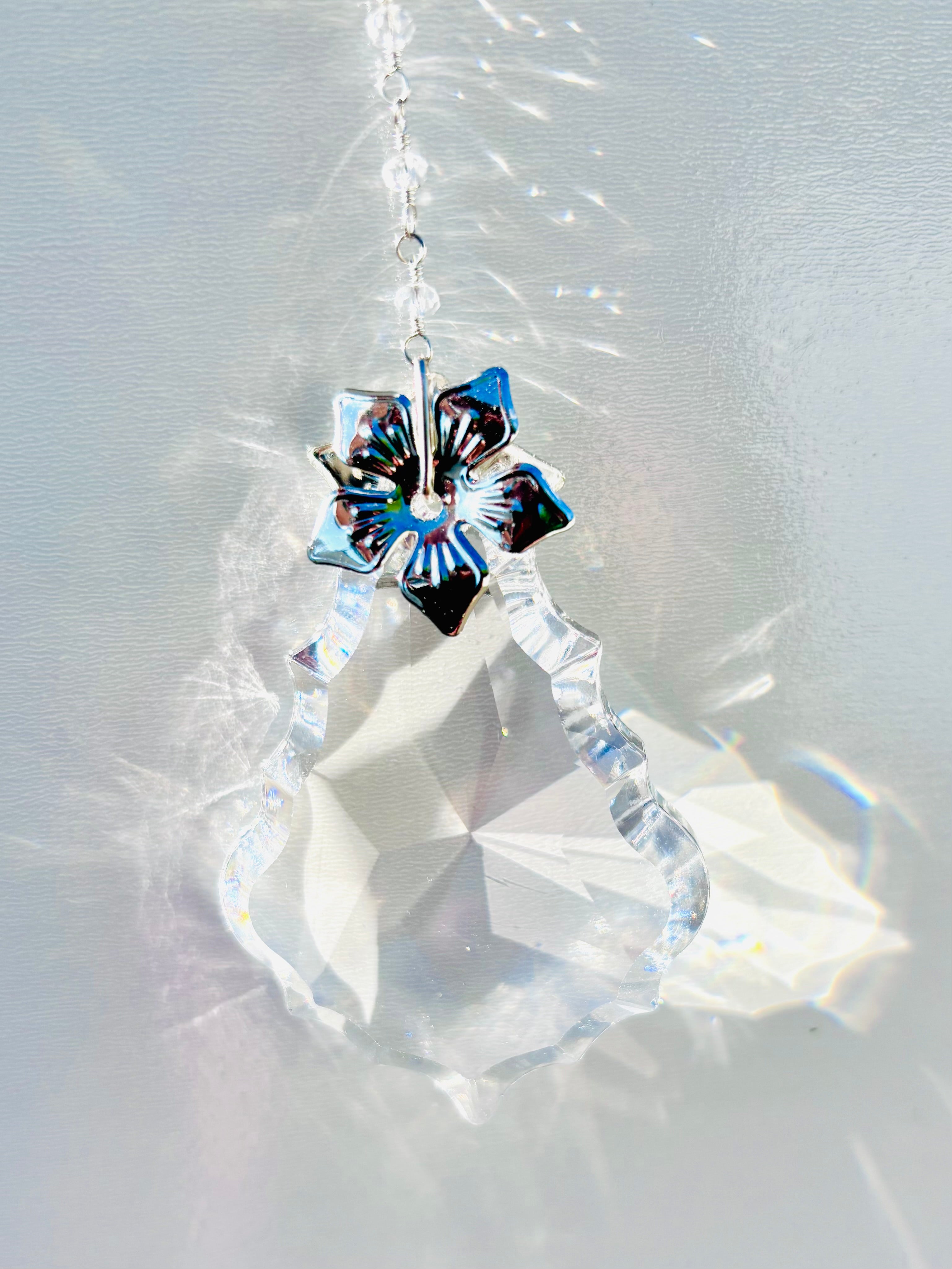 Diamond like suncatcher featuring a silver flower and portraying glowing rainbows around it. 