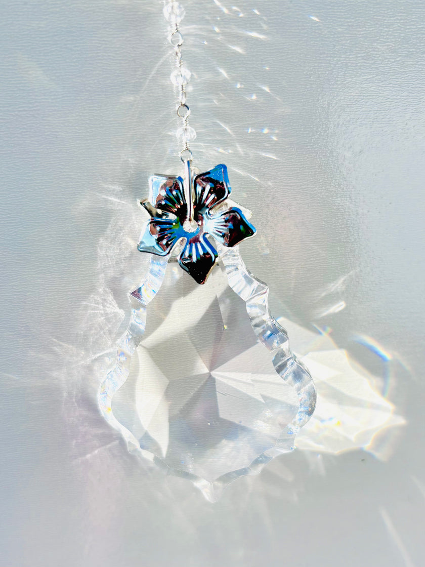 Diamond like suncatcher featuring a silver flower and portraying glowing rainbows around it. 