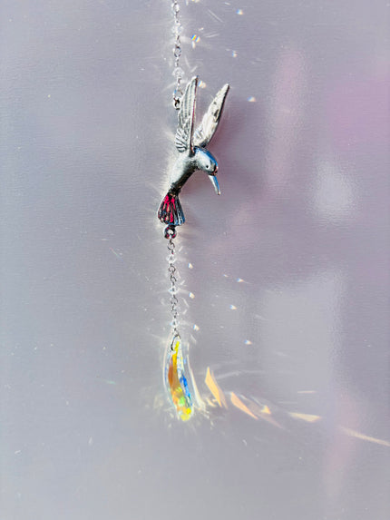 Colorful hummingbird-shaped ornament hanging from a with a Swarovski crystal creating rainbows.