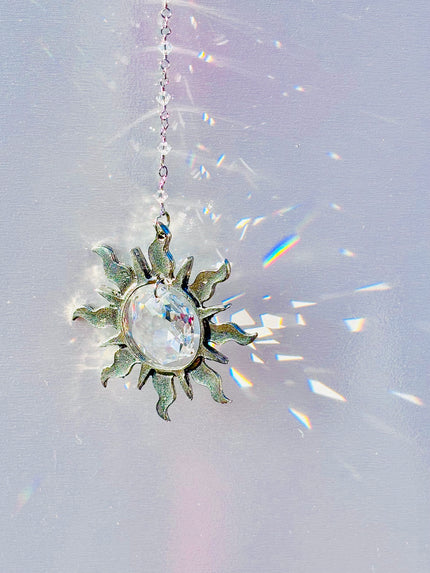 Decorative sun-shaped crystal hanging on a chain with rainbow prisms.