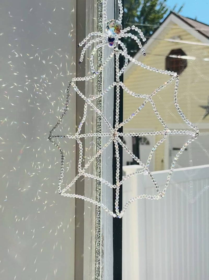 Video preview of the Amara Collection crystal spider and web suncatcher hanging in a window frame. The camera moves slightly to show how the 448 hand-beaded glass crystals and large faceted Swarovski spider catch the natural daylight, casting brilliant, shimmering reflections.