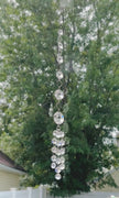 Handmade Neptune’s Octagon Prism crystal suncatcher spinning in a window against a background of lush green trees, capturing bright sunlight lighting it up through its clear faceted glass prisms.