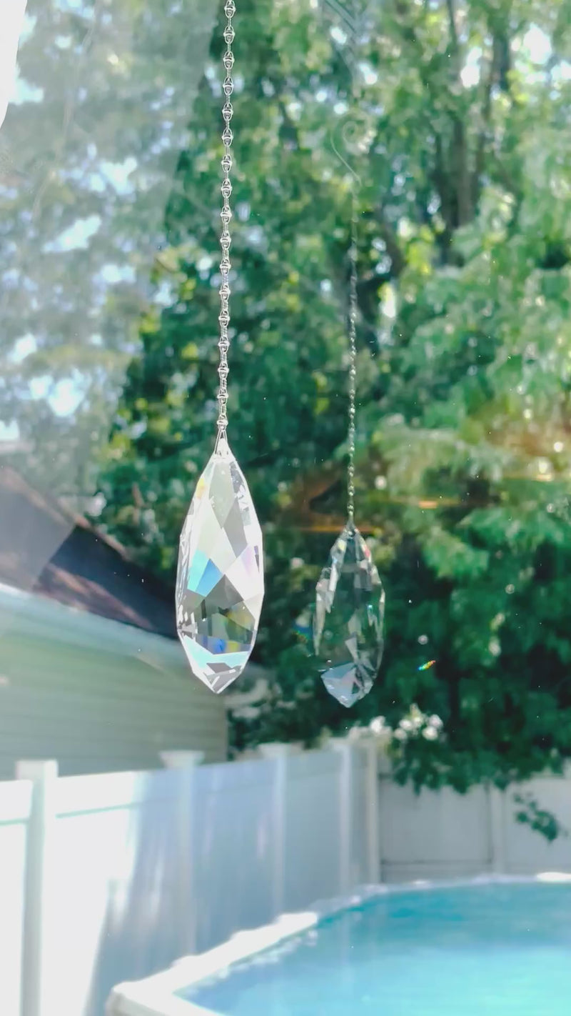 A large faceted suncatcher with a colorful Swarovski crystal sparkling as it is spinning in a bright window casting its own reflection.