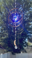 Artisan Serene Orbit crystal suncatcher spinning gently as its central Swarovski prism shifts and changes colors from iridescent blue to bright green in the sunlight.