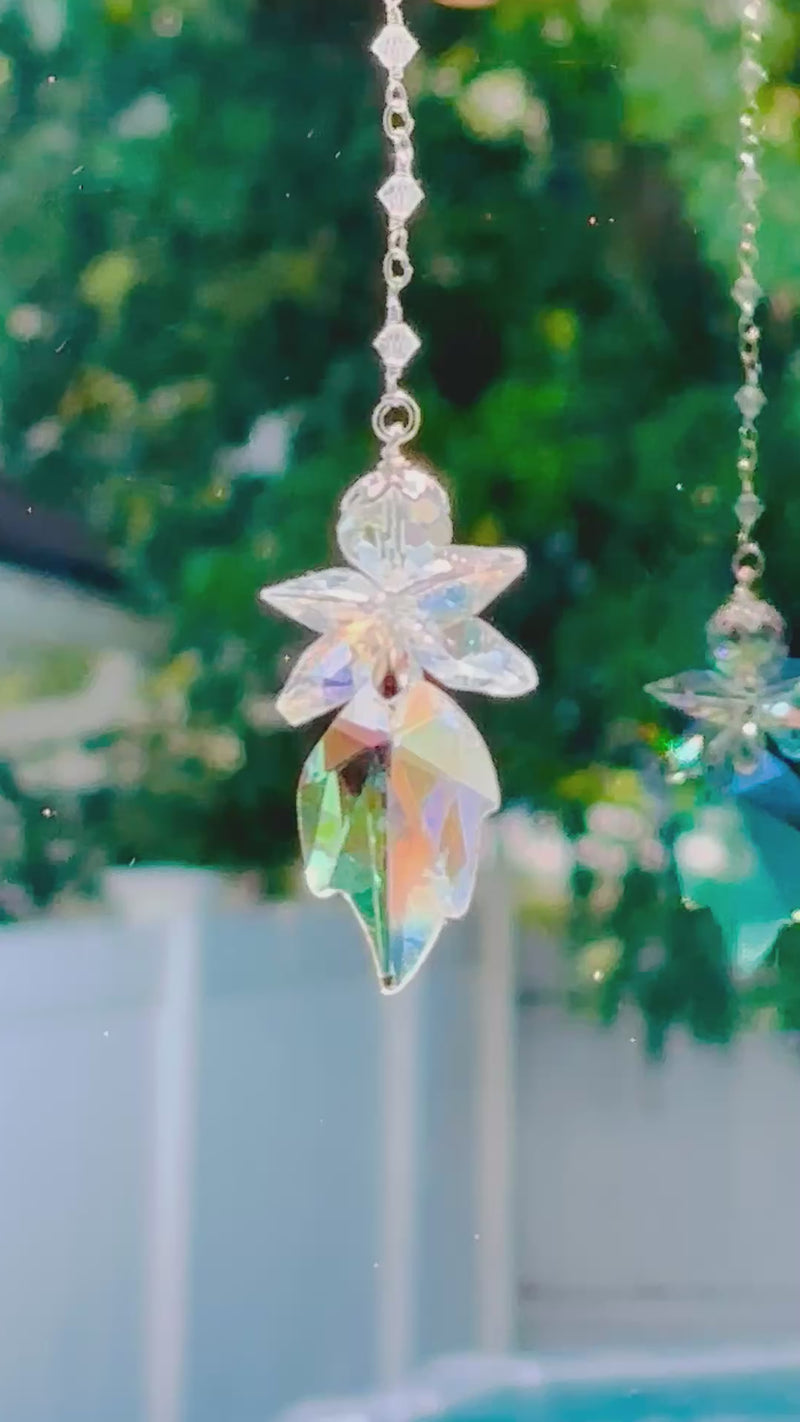 A colorful crystal fairy spinning in a bright window shooting prisms and its own reflection.