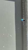 Handcrafted Hopea crystal angel suncatcher spinning gently in bright sunlight, showing a side view of its smoky metallic wings and long faceted prism body casting vibrant prisms.