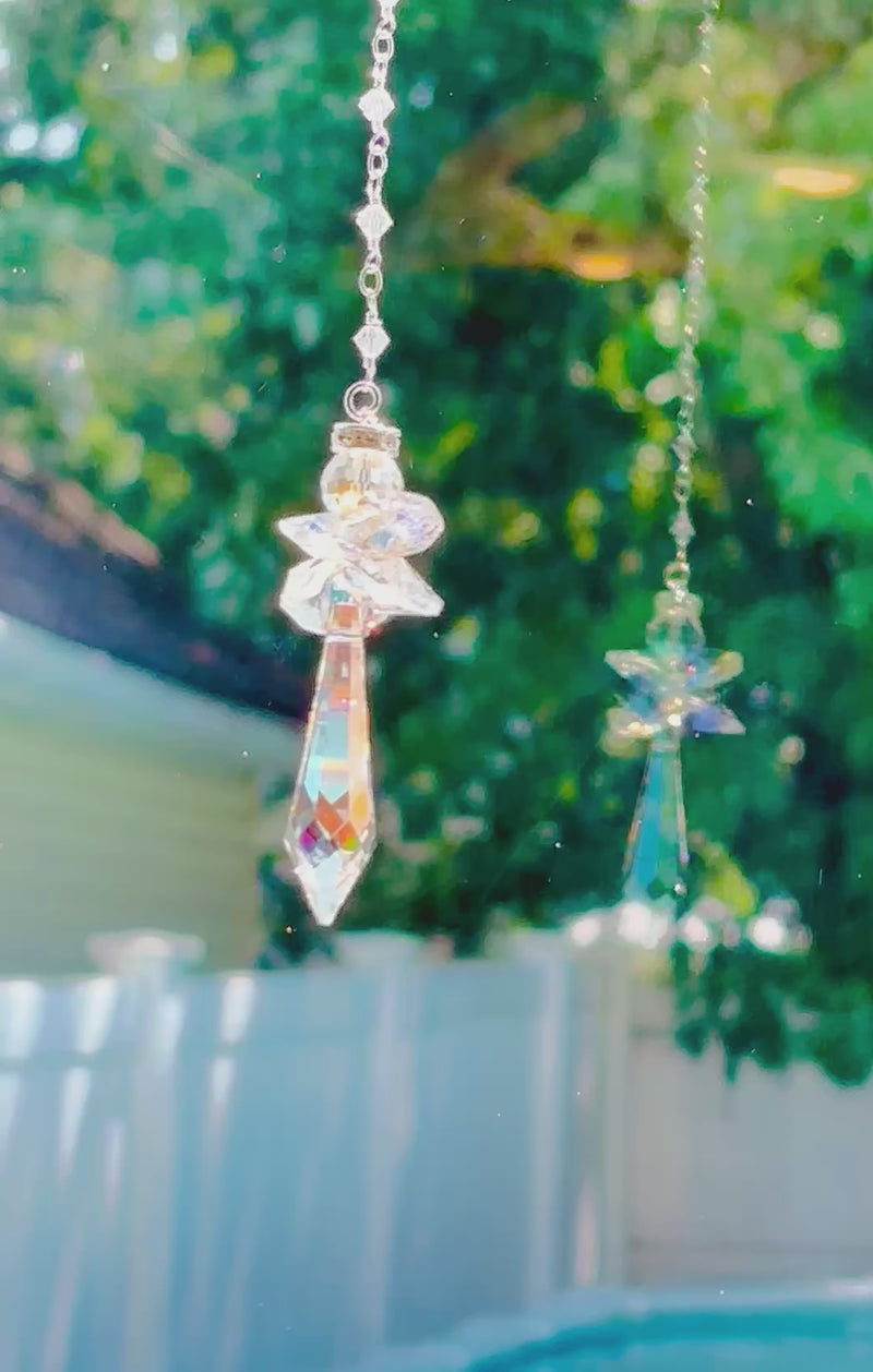 An Aurora borealis angel suncatcher casting prisms and it’s reflection in a bright window.
