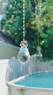 A handmade suncatcher with a colorful crystal sparkling as it is spinning in a bright window casting its own reflection.