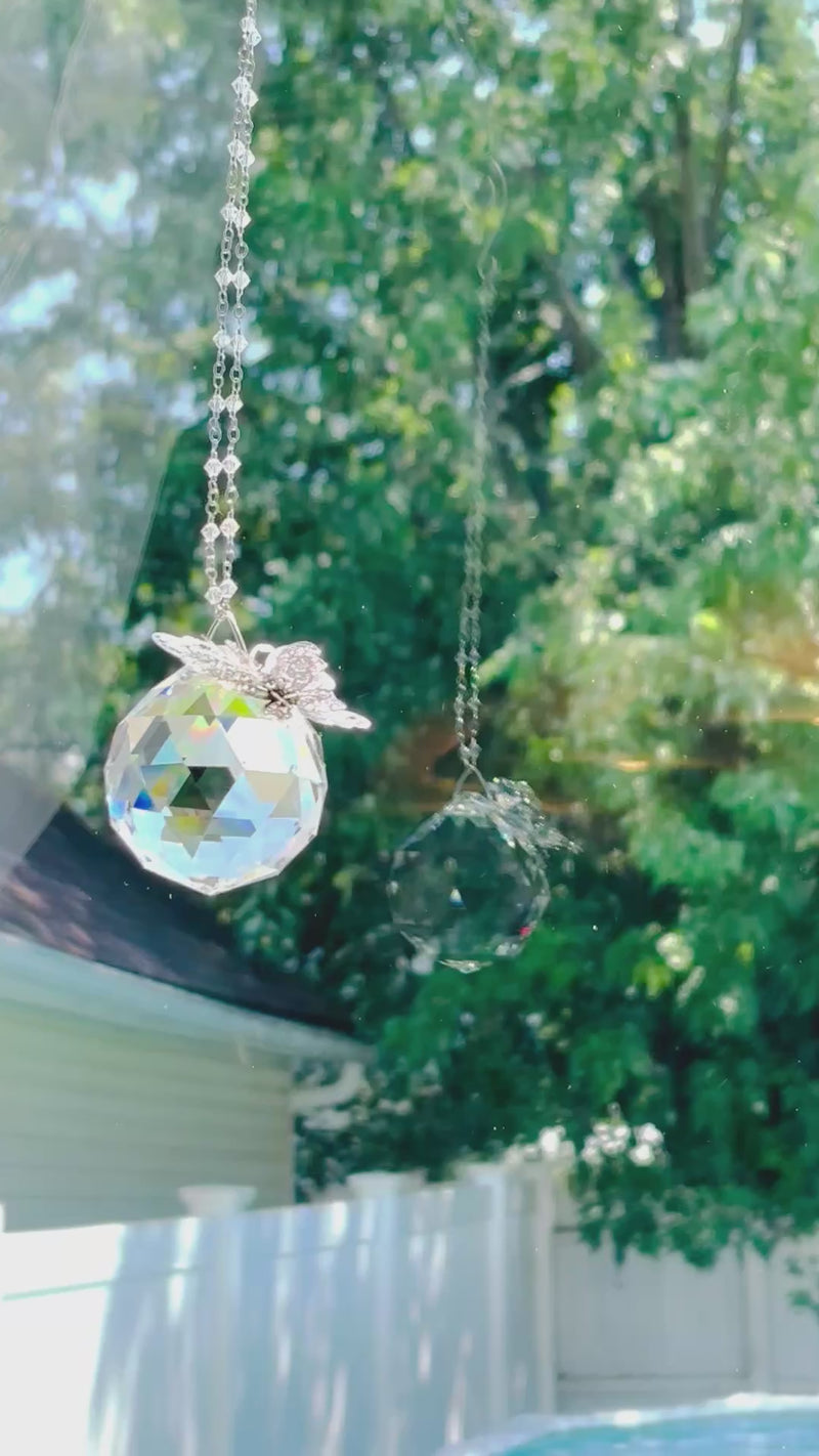 A large suncatcher with a colorful Swarovski crystal sparkling as it is spinning in a bright window casting its own reflection.