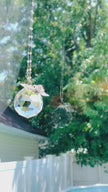 A large suncatcher with a colorful Swarovski crystal sparkling as it is spinning in a bright window casting its own reflection.