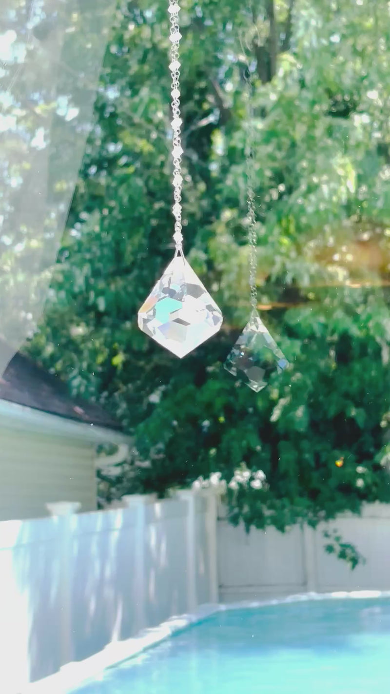 A large suncatcher with a colorful Swarovski crystal sparkling as it is spinning in a bright window casting its own reflection.
