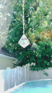 A large suncatcher with a colorful Swarovski crystal sparkling as it is spinning in a bright window casting its own reflection.