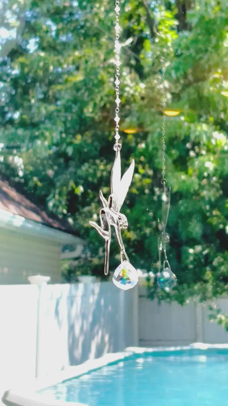 A fairy suncatcher with a colorful Swarovski crystal sparkling as it is spinning in a bright window casting its own reflection.